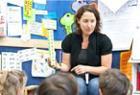 Female teacher, in front of a class of primary age children, displays a visual chart