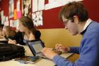 A senior secondary student, who uses a hearing aid, works on a laptop in a classroom setting