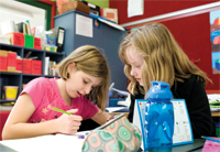 Two primary age school children in a classroom setting, working together on a written exercise Two primary age school children in a classroom setting, working together on a written exercise
