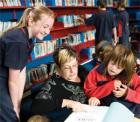 An adult educator reads to a group of children in a library setting An adult educator reads to a group of children in a library setting