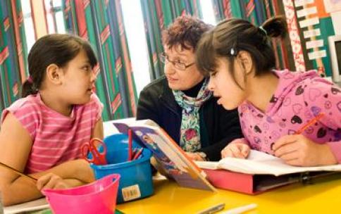A teachers works with two primary age students on a reading and writing activity