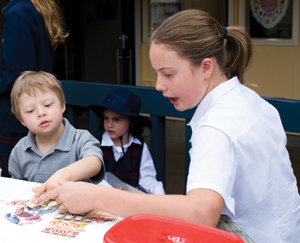 A primary age child is reading with a book in the playground with a junior primary age child A primary age child is reading with a book in the playground with a junior primary age child