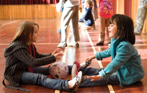 Two primary age children are sitting in a gymnasium floor, rolling a ball between them Two primary age children are sitting in a gymnasium floor, rolling a ball between them
