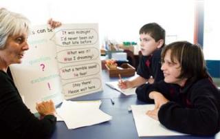 A teacher guiding two primary age students in a reading and writing exercise, at a table. A teacher guiding two primary age students in a reading and writing exercise, at a table.